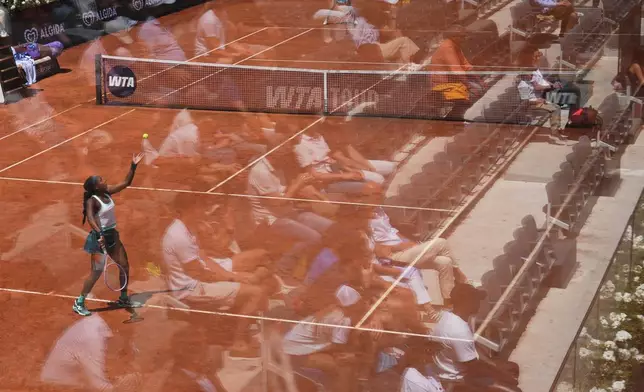 Fans are reflected in a glass partition as Coco Gauff, of the United States, serves the ball to United States' Iva Jovic during their match at the Italian Open tennis tournament in Rome, Monday, May 11, 2026. (AP Photo/Alessandra Tarantino)