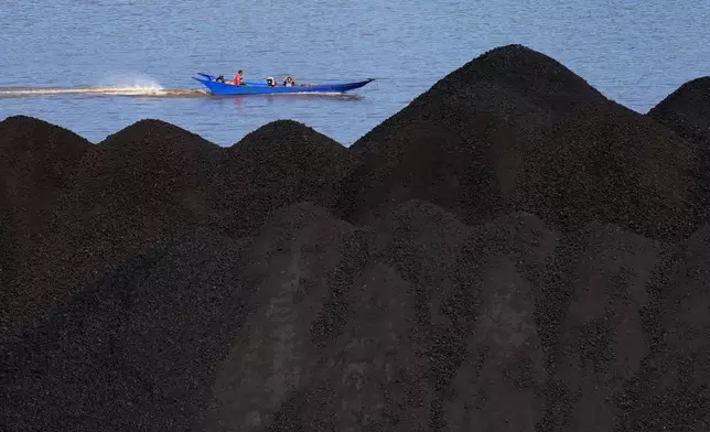 FILE - A boat cruises past a coal piled up on a barge on Mahakam River in Samarinda, East Kalimantan, Indonesia, Dec. 19, 2022. (AP Photo/Dita Alangkara, File)