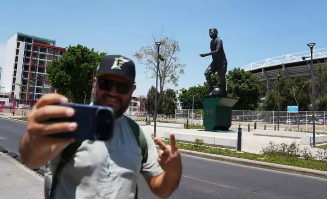 A fan takes a picture with a statue of Brazilian soccer player in the background after its unveiling outside Jalisco Stadium in Guadalajara, Mexico, Thursday, May 21, 2026. (AP Photo/Refugio Ruiz)