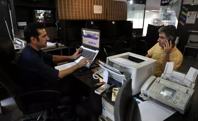 FILE - An internet cafe manager works on his computer as a man talks on his cell phone in Tehran, Iran, July 25, 2019. (AP Photo/Vahid Salemi, File)
