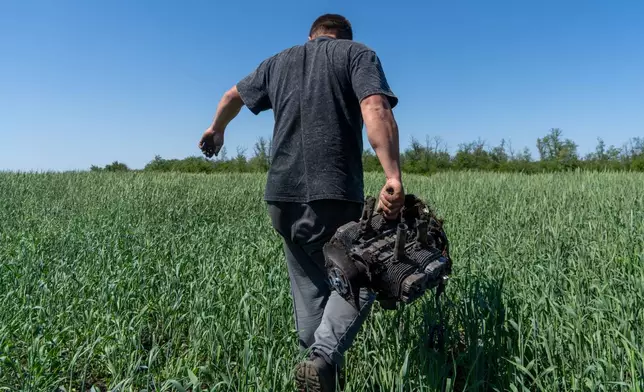A farmer carries a fragment of a Russian drone on an agricultural field near the front line in the Kharkiv region, Ukraine, Friday, May 22, 2026. (AP Photo/Andrii Marienko)