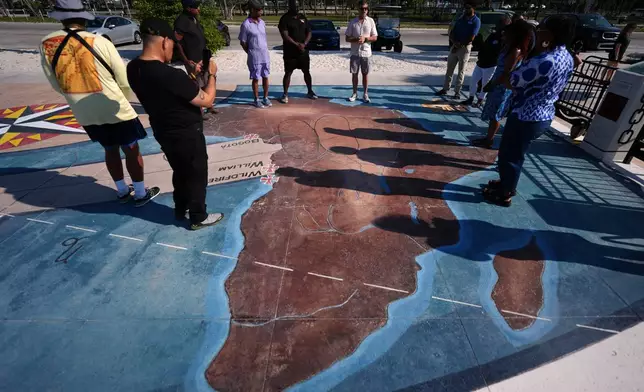 Corey Malcom, center, lead historian with the Florida Keys History Center, talks to Black divers from the Underwater Adventure Seekers, as they visit a memorial built on the site where hundreds of Africans who died in 1860 after being rescued from three slave ships were buried, on Higgs Beach in Key West, Fla., Saturday, May 9, 2026. (AP Photo/Rebecca Blackwell)