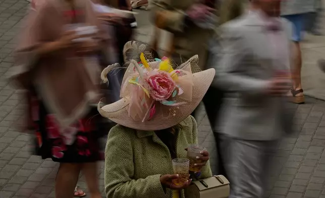 A woman holds drinks as people pass before the 152nd running of the Kentucky Derby horse race at Churchill Downs, Saturday, May 2, 2026, in Louisville, Ky. (AP Photo/Charlie Riedel)