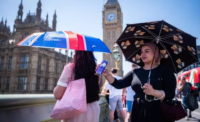 Tourists shelter from the sun beneath umbrellas during the hot weather on Westminster Bridge, central London, England, Monday, May 25, 2026. (James Manning/PA via AP)