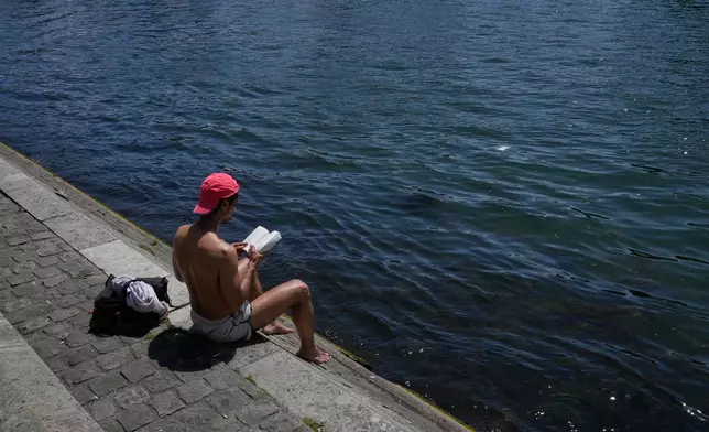 A man reads a book while sitting in the sun along the Seine River in Paris, Monday, May 25, 2026. (AP Photo/Michel Euler)
