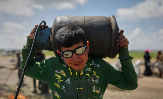 A worker carries a gas cylinder used to fuel burners that roast green wheat to produce freekeh, a roasted green wheat grain widely used in Levantine cuisine and made by harvesting immature wheat and roasting it over open flames to separate and preserve the grains, on the outskirts of Taftanaz, northwestern Syria, Sunday, May 24, 2026. (AP Photo/Ghaith Alsayed)