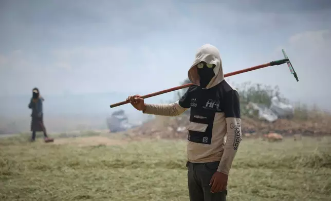 A laborer pauses with his rake as Syrian workers burn green wheat to produce freekeh, a roasted green wheat grain widely used in Levantine cuisine and made by harvesting immature wheat and roasting it over open flames to separate and preserve the grains, on the outskirts of Taftanaz, northwestern Syria, Sunday, May 24, 2026. (AP Photo/Ghaith Alsayed)