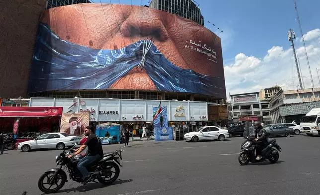 Vehicles drive past a billboard with graphic showing Strait of Hormuz and sewn lips of U.S. President Donald Trump in a square in downtown Tehran, Iran, Saturday, May 2, 2026. (AP Photo/Vahid Salemi)
