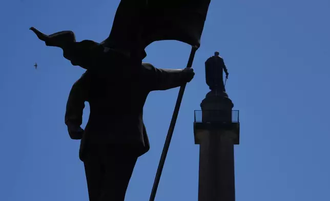 A statue of a man holding a flag which covers his face, left, and signed 'Banksy, has appeared in Waterloo Place in London, Thursday, April 30, 2026. (AP Photo/Kin Cheung)