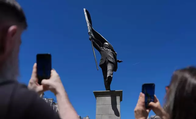 Members of the public look at a statue of a man holding a flag covering his face, and signed 'Banksy', which has appeared in Waterloo Place in London, Thursday, April 30, 2026. (AP Photo/Kin Cheung)