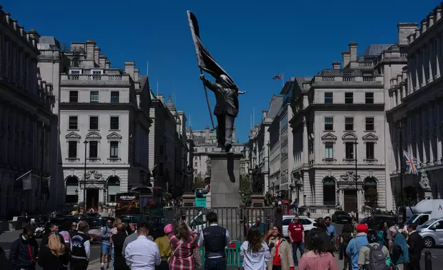Members of the public look at a statue of a man holding a flag covering his face, and signed 'Banksy', which has appeared in Waterloo Place in London, Thursday, April 30, 2026. (AP Photo/Kin Cheung)