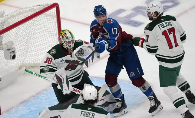 Colorado Avalanche center Parker Kelly, center top, tries to redirect a shot at Minnesota Wild goaltender Jesper Wallstedt (30) as Wild left wing Marcus Foligno, right, covers in the first period of Game 1 of an NHL hockey Stanley Cup second-round playoff series Sunday, May 3, 2026, in Denver. (AP Photo/David Zalubowski)