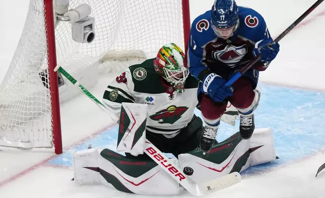 Colorado Avalanche center Parker Kelly, right, jumps as Minnesota Wild goaltender Jesper Wallstedt makes a stick save of a shot in the third period of Game 1 of an NHL hockey Stanley Cup second-round playoff series Sunday, May 3, 2026, in Denver. (AP Photo/David Zalubowski)