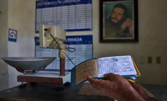 A man shows his ration book known as a "libreta," backdropped by a framed image of Fidel Castro, at a state-run bodega in Havana, Cuba, Saturday, May 2, 2026. (AP Photo/Ramon Espinosa)
