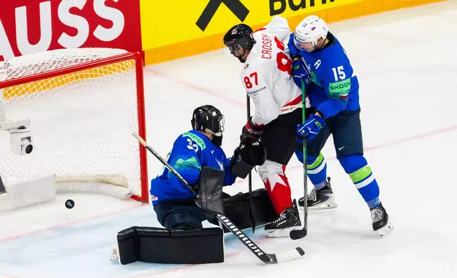 Slovenia's goaltender Zan Us, left, concedes his second goal past Slovenia's Blaz Gregorc, right, and Canada's Sidney Crosby, center, during a preliminary round game between Canada and Slovenia at the men's ice hockey world championship in Fribourg, Switzerland, Friday May 22, 2026. (Salvatore Di Nolfi/Keystone via AP)