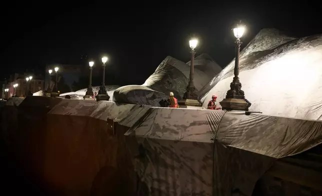 A worker monitors the inflation of "The Pont Neuf Cave" by French street artist JR on the Pont Neuf bridge in Paris on Wednesday, May 20, 2026, before its free public opening from June 6 to 28. (AP Photo/Thomas Padilla)