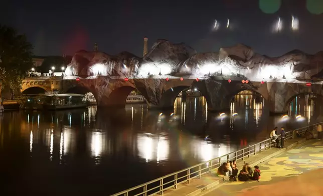 Inflation of the artwork "The Pont Neuf Cave" by French street artist JR on the Pont Neuf bridge, with the Eiffel Tower behind it, Wednesday, May 20, 2026, in Paris, before its free opening to the public from June 6 to 28. (AP Photo/Thomas Padilla)