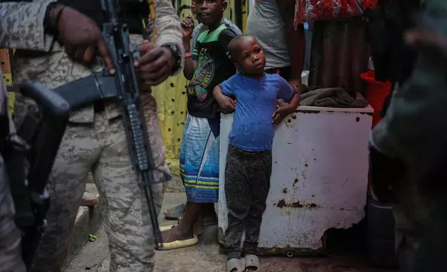 FILE - Children stand next to police officers during a visit from World Food Programme advisor Princess Sarah Zeid of Jordan at a shelter for families displaced by gang violence in Port-au-Prince, Haiti, Monday, April 27, 2026. (AP Photo/Odelyn Joseph, File)
