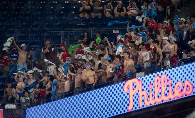 A group of fans in the upper deck wave their shirts as they go "tarps off" during the eighth inning of a baseball game between the Cincinnati Reds and the Philadelphia Phillies, Tuesday, May 19, 2026, in Philadelphia. (AP Photo/Chris Szagola)