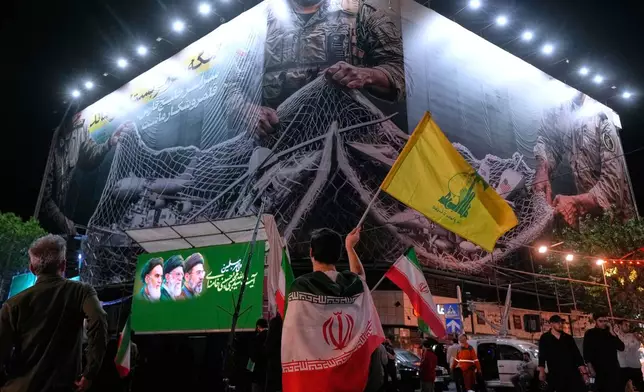 An Iranian demonstrator waves a flag of Lebanon's militant Hezbollah group under an anti-U.S. billboard depicting the American aircrafts into the Iranian armed forces fishing net with signs that read in Farsi: "The Strait of Hormuz will remain closed, The entire Persian Gulf is our hunting ground," during a pro-government gathering at Enqelab-e-Eslami, or Islamic Revolution, square in Tehran, Iran, Monday, May 4, 2026. (AP Photo/Vahid Salemi)