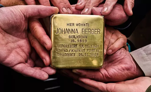 Relatives shows a photo a palm-sized brass Holocaust plaque reading "Johanna Berger, born in 1893, lived here; deported on Nov. 17, 1941, murdered on Nov. 25, 1941 in Kowno/Kaunas Fort IX" by artist Gunter Demnig prior to the placing of the so called "Stolperstein" or "Stumbling Blocks" in front of her former home in Berlin, Germany, Wednesday, May 6, 2026. (AP Photo/Markus Schreiber)