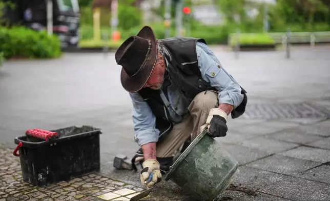 Artist Gunter Demnig places a palm-sized brass Holocaust plaques called "Stolpersteine", or "Stumbling Blocks" with the names of victims of the Nazi regime in front of their former home at a street in Berlin, Germany, Wednesday, May 6, 2026. (AP Photo/Markus Schreiber)