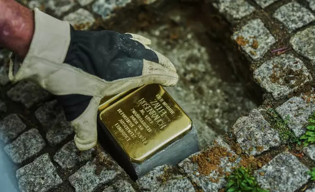 Artist Gunter Demnig places a palm-sized brass Holocaust plaque called "Stolpersteine", or "Stumbling Blocks" with the inscription " Zallel Rosenrauch, born in 1893, lived here; forced labourer at DUCO AG; deported on 3 March 1943; murdered in Auschwitz" front of her former home in Berlin, Germany, Wednesday, May 6, 2026. (AP Photo/Markus Schreiber)