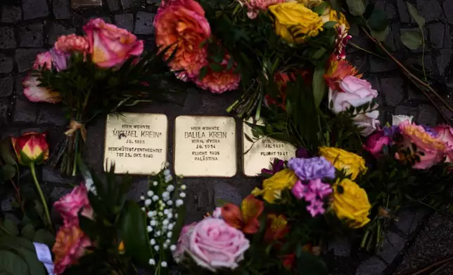 Flowers lay near palm-sized brass Holocaust plaques of the Krein family, after the so called "Stolpersteine", or "Stumbling Blocks" by artist Gunter Demnig, in Berlin, Germany, Wednesday, May 6, 2026. (AP Photo/Markus Schreiber)