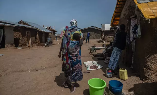 A woman carrying a child walks through the camp on the property of the city's ISP (Institut Supérieur Pédagogique), where internally displaced people reside in Bunia, Congo, Tuesday, May 26, 2026. (AP Photo/Moses Sawasawa)