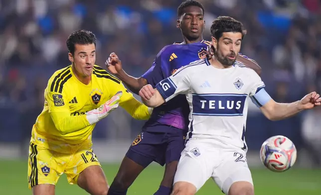Los Angeles Galaxy goalkeeper James Marcinkowski (12) watches as defender Emiro Garces, center, and Vancouver Whitecaps forward Brian White fight for the ball during the first half of an MLS soccer match Saturday, May 2, 2026, in Carson, Calif. (AP Photo/Jae C. Hong)