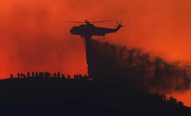 A water tanker drops water while firefighters walk below, as the Sandy Fire approaches, Tuesday, May 19, 2026, in Simi Valley, Calif. (AP Photo/Caroline Brehman)