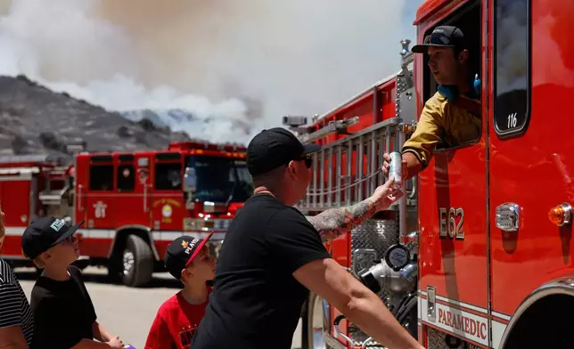 Matt Brantley and his kids hand a firefighter a drink during wildfires, Tuesday, May 19, 2026, in Simi Valley, Calif. (AP Photo/Caroline Brehman)