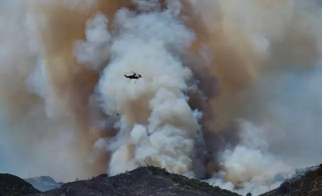 A helicopter drops water on wildfires, Tuesday, May 19, 2026, in Simi Valley, Calif. (AP Photo/Caroline Brehman)