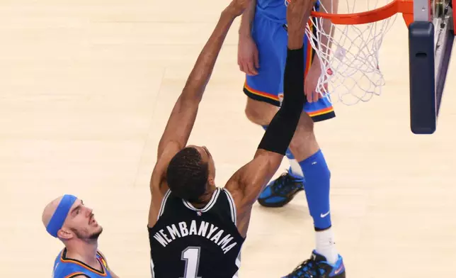 San Antonio Spurs forward Victor Wembanyama (1) dunks against Oklahoma City Thunder guard Alex Caruso, left, and center Chet Holmgren (7) during double overtime of Game 1 in a third-round NBA basketball playoffs series Monday, May 18, 2026, in Oklahoma City. (AP Photo/Nate Billings)
