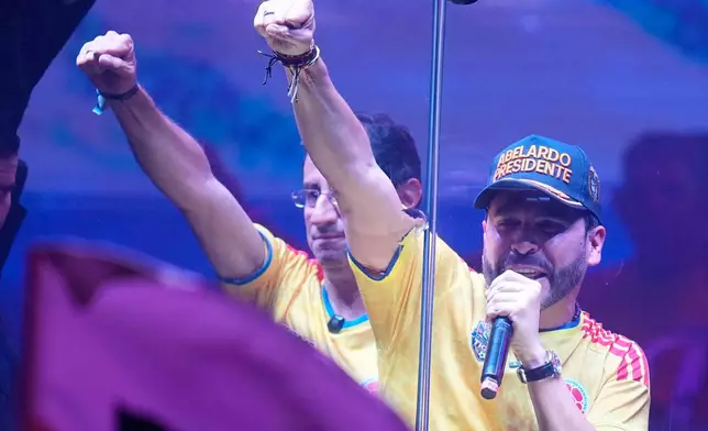 Presidential candidate Abelardo de la Espriella of the Defenders of the Motherland movement and his running mate Jose Manuel Restrepo, left, raise their fit from behind a bullet proof booth during a campaign rally in Barranquilla, Colombia, Saturday, May 23, 2026. (AP Photo/Fernando Vergara)