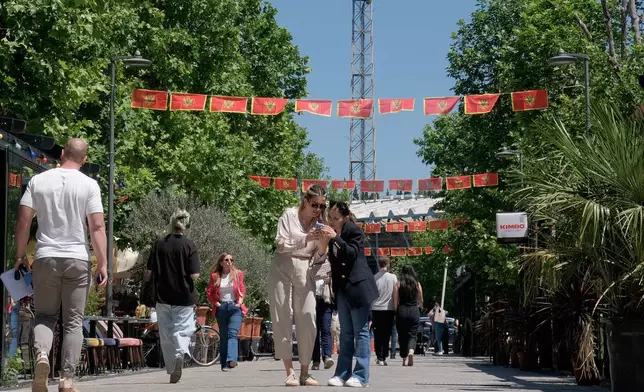 Pedestrians walk on a street decorated with national flags in Montenegro's capital Podgorica, Monday, May 18, 2026. (AP Photo/Risto Bozovic)