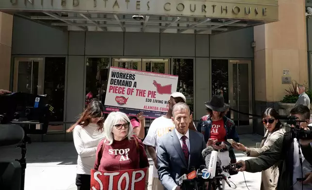 Marc Toberoff, attorney for Elon Musk, bottom middle, speaks to reporters outside the U.S. District Court, Monday, May 18, 2026, in Oakland, Calif. (AP Photo/Nathan Weyland)