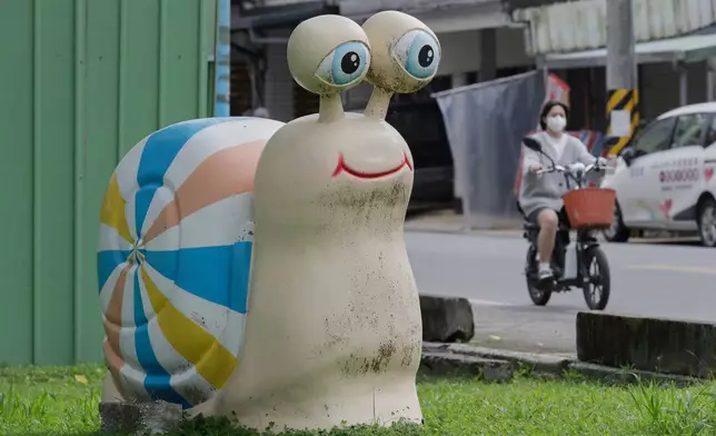 A woman rides a bike past a statue of a snail in Fenglin town, Hualien County, eastern of Taiwan, Saturday, May 2, 2026. (AP Photo/Chiang Ying-ying)
