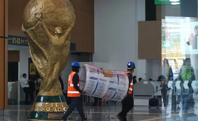 Workers transport a roll of foam next to the FIFA World Cup trophy during a guided media tour of the renovation site at Benito Juárez International Airport, in preparation for the 2026 World Cup, in Mexico City, on Tuesday, May 19, 2026. (AP Photo/Fernando Llano)