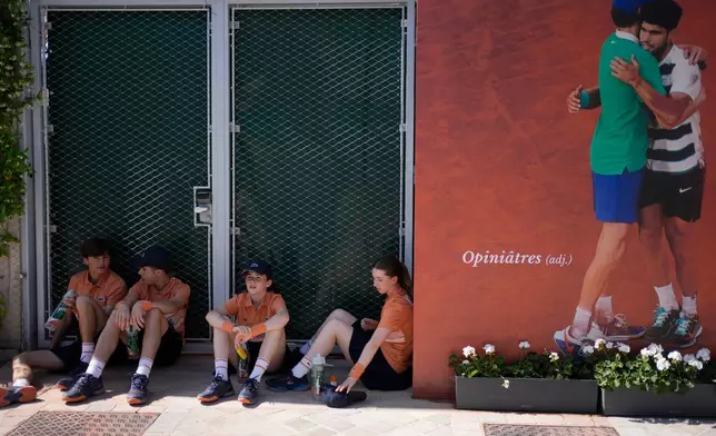 Ballboys and ballgirls cover themselves of the sun in a shade at the French Open tennis tournament in Paris, Tuesday, May 26, 2026. (AP Photo/Christophe Ena)