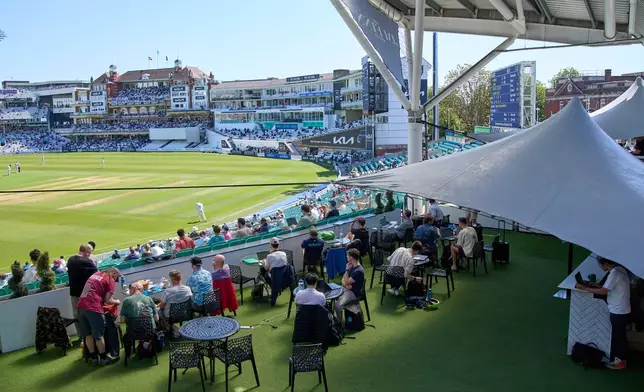 People work and watch cricket during a Surrey against Sussex County Championship cricket match at the Kia Oval in London, Friday, May 1, 2026. (AP Photo/Tony Hicks)