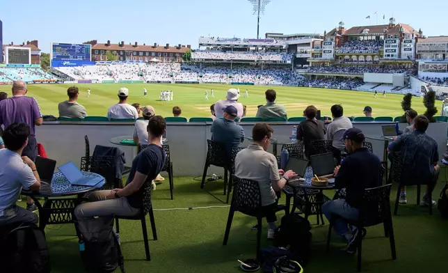 People work and watch cricket during a Surrey against Sussex County Championship cricket match at the Kia Oval in London, Friday, May 1, 2026. (AP Photo/Tony Hicks)