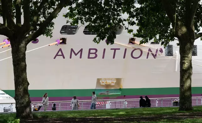 People walk past the British cruise ship Ambition as French authorities have ordered 1,700 passengers and crew to stay on board due to a gastrointestinal illness outbreak, in Bordeaux, southwestern France, Wednesday, May 13, 2026. (AP Photo/Caroline Blumberg)