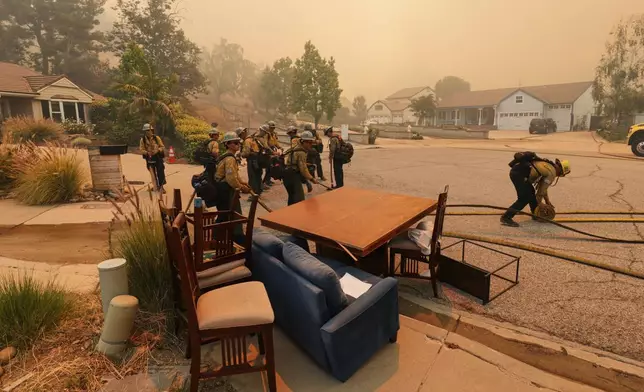 Fire crews roll out hoses at a cul-de-sac while battling the Sandy Fire Monday, May 18, 2026, in Simi Valley, Calif. (AP Photo/Ethan Swope)