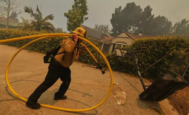 A firefighter sets up hoses while battling the Sandy Fire Monday, May 18, 2026, in Simi Valley, Calif. (AP Photo/Ethan Swope)