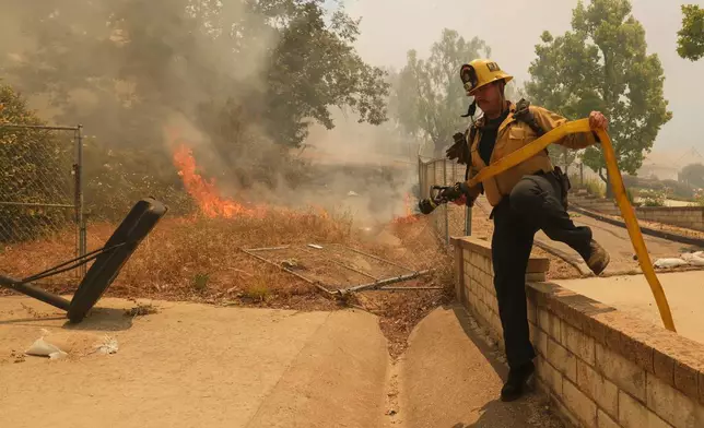 A firefighter hops over a fence while battling the Sandy Fire Monday, May 18, 2026, in Simi Valley, Calif. (AP Photo/Ethan Swope)