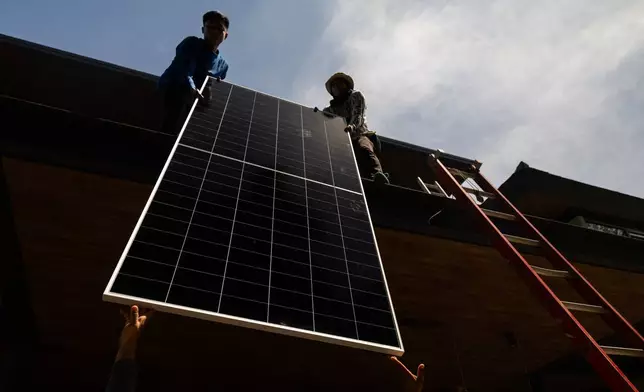 A team of solar installers haul a solar panel onto the roof of a home in Manila, Philippines, on April 30, 2026. (AP Photo/Anton L. Delgado)