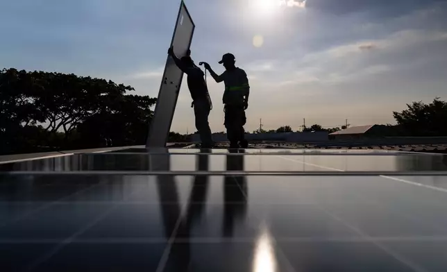 A pair of solar installers haul a solar panel onto the roof of a home in Manila, Philippines, on April 30, 2026. (AP Photo/Anton L. Delgado)