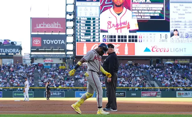 Atlanta Braves' Ronald Acuña Jr., center left, walks gingerly after being injured while running out a groundout as first base umpire Bill Miller, center right, looks on in the second inning of a baseball game against the Colorado Rockies, Saturday, May 2, 2026, in Denver. (AP Photo/David Zalubowski)