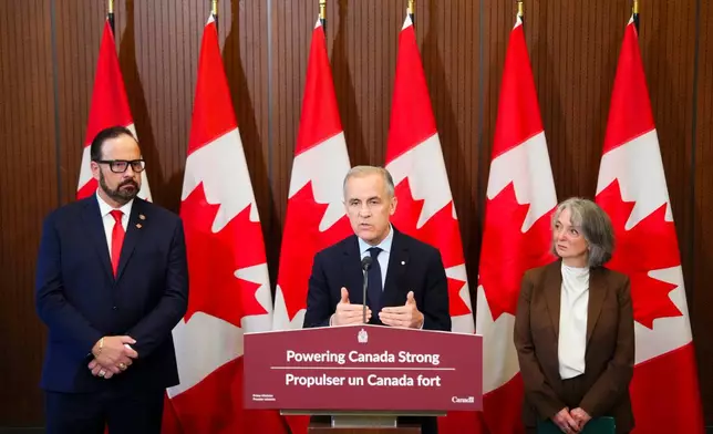 Prime Minister Mark Carney makes an announcement accompanied by Russ Shewchuk International Vice -President for International Brotherhood of Electrical Workers (IBEW) First District, left, and Minister of Environment and Climate Change Julie Dabrusin, right, on Parliament Hill in Ottawa on Thursday, May 14, 2026. (Sean Kilpatrick/The Canadian Press via AP)